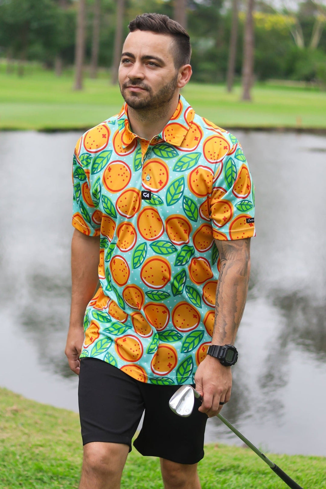 Orange print golf shirt with black shorts and white watch.