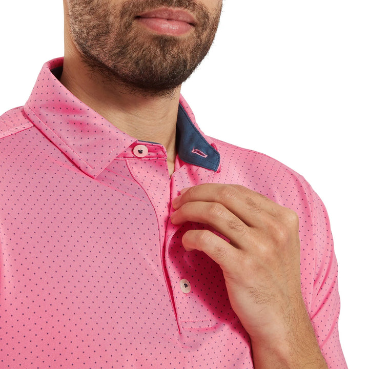 Pink polo shirt with small polka dots and navy blue collar, made of cotton.
